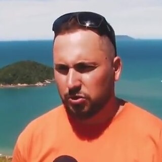 Felipe da Silva, de camiseta da Parapente Ilha da Magia, com o mar da Praia de Palmas ao fundo